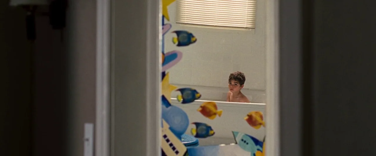 Mirrors (2008) movie still: medium — A view through a door shows a boy in a bathtub inside a bathroom. Decorative fish-shaped stickers are placed on…