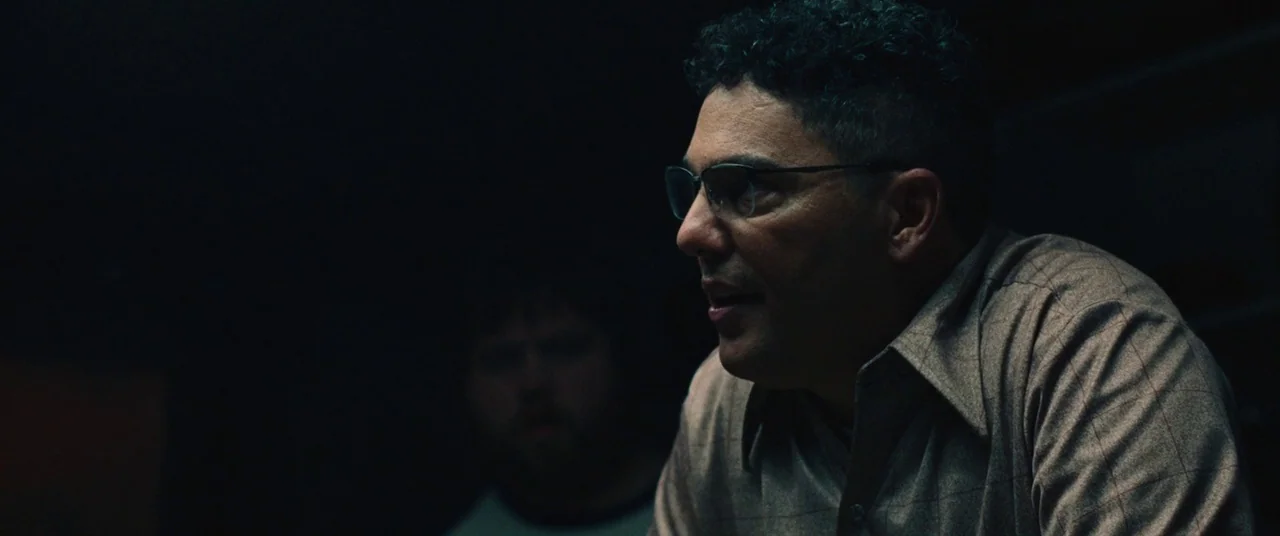 BlacKkKlansman (2018) movie still: medium — A man sits in a dark, indistinct interior setting with minimal ambient light. He is partially lit while…
