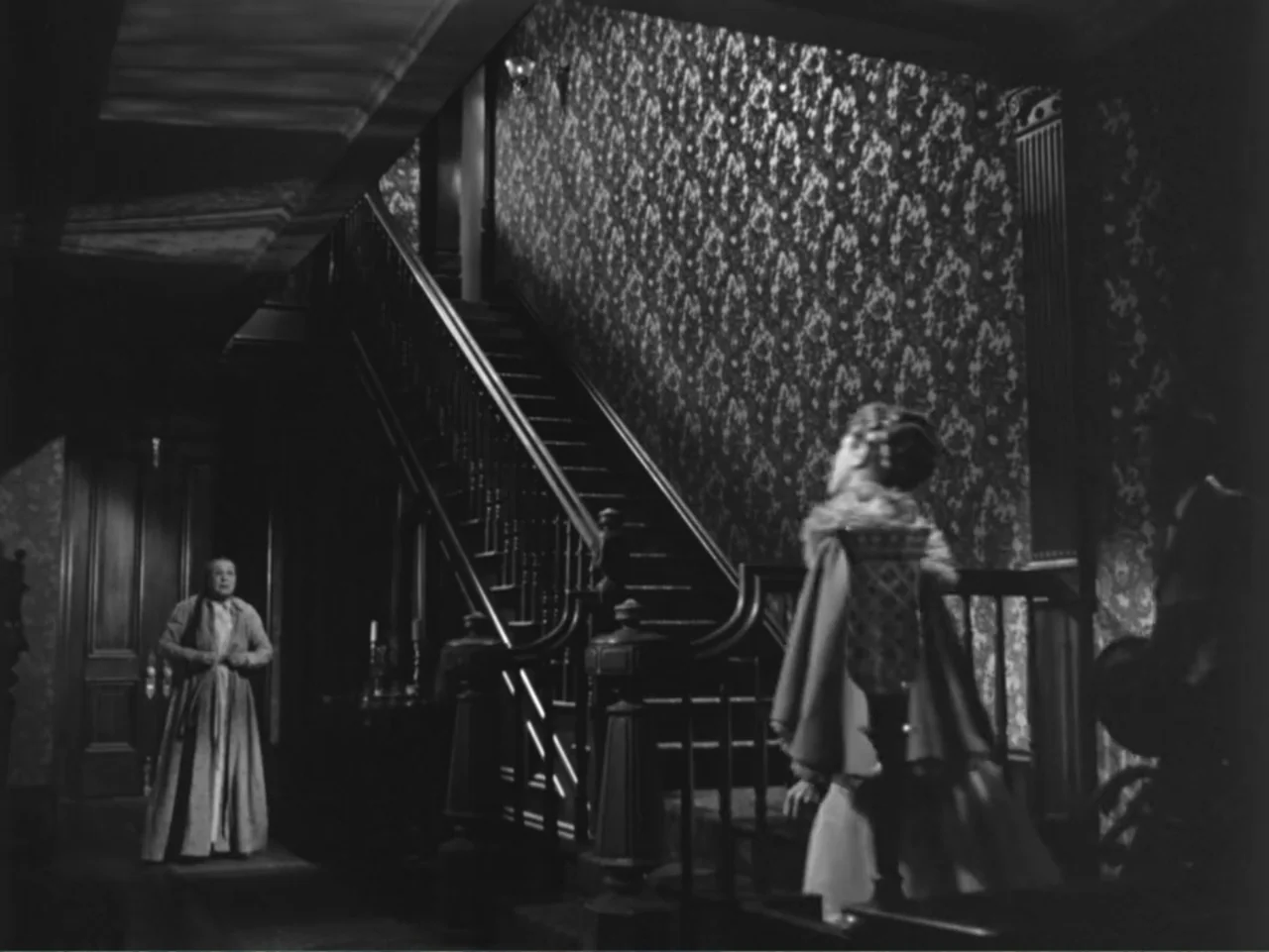 House by the River (1950) movie still: medium — A dark foyer features a prominent wooden staircase and ornate patterned wallpaper in black and…