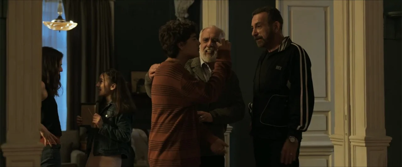 Dive (2013) movie still: medium — A dimly lit room with dark walls and a doorway frame. Four people are standing together engaged in conversation.