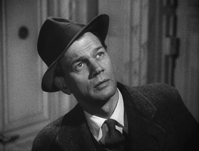 The Third Man (1949) movie still: closeup — A man stands indoors against a wall with simple paneling. He looks toward the side while wearing a hat…