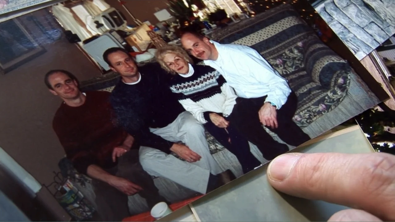 The Cheshire Murders (2013) movie still: medium — A vintage physical photograph shows four people sitting on a floral pattern sofa. The people are…