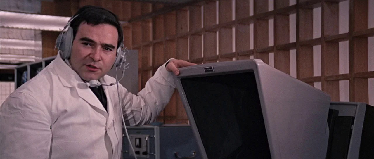 You Only Live Twice (1967) movie still: medium — A technical room features a large gray computer terminal and a wooden lattice wall. A man in a…