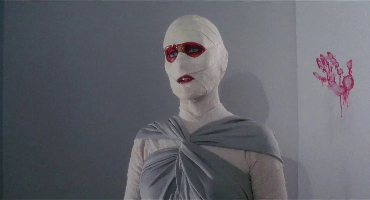 Hellbound: Hellraiser II (1988) movie still: medium — A figure in bandages stands against a blank white wall with a bloody print. The individual…
