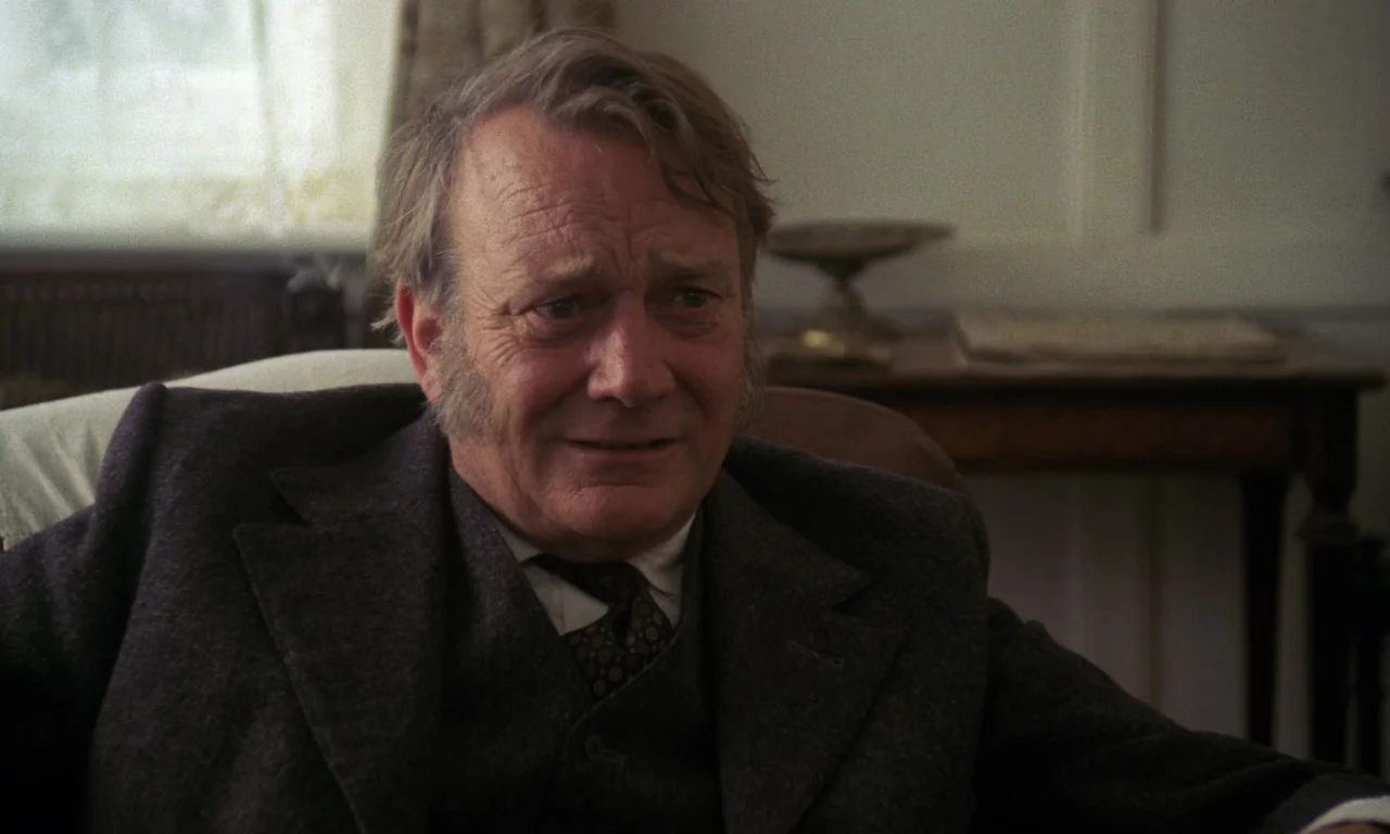 A Room With A View (1985) movie still: medium — A well-lit sitting room contains a wooden table and a window with light curtains. An older man…