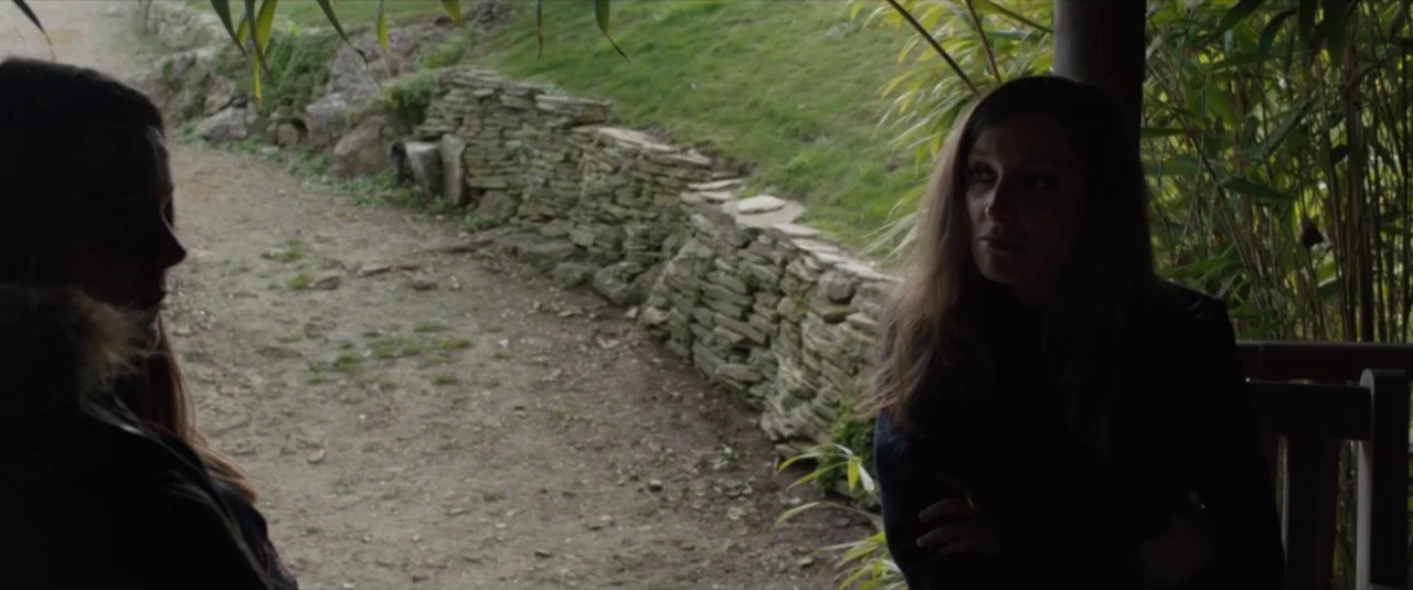 Happy New Year, Colin Burstead (2018) movie still: medium — A partially shaded patio overlooks a dirt path lined with a dry stone wall. Two women…