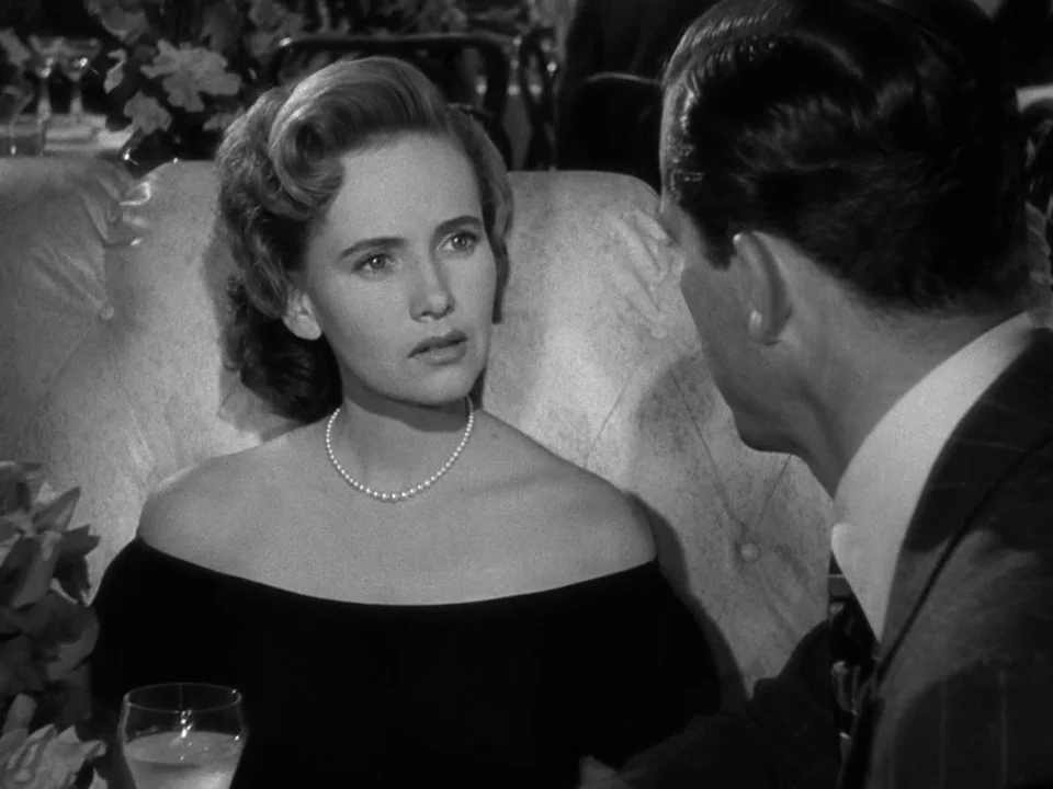 The Best Years of Our Lives (1946) movie still: medium — A dark restaurant booth with tufted upholstery and a glass on the table. A woman in a black…