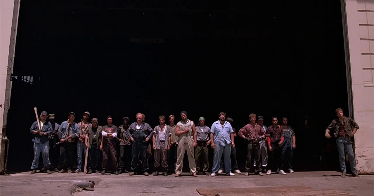 Darkman (1990) movie still: wide — A group of laborers stands in a long horizontal line against a massive dark void. The scene is set at the…