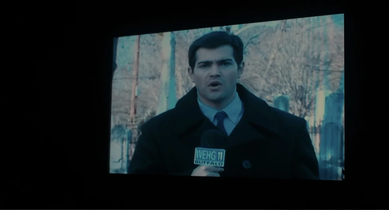 Beyond a Reasonable Doubt (2009) movie still: medium — A man stands outdoors in front of a blurred cemetery background. The reporter speaks directly…