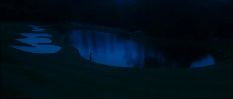 Mother (2009) movie still: wide — A dark golf course at night features a pond with surrounding grass sand traps. A solitary figure stands at the…