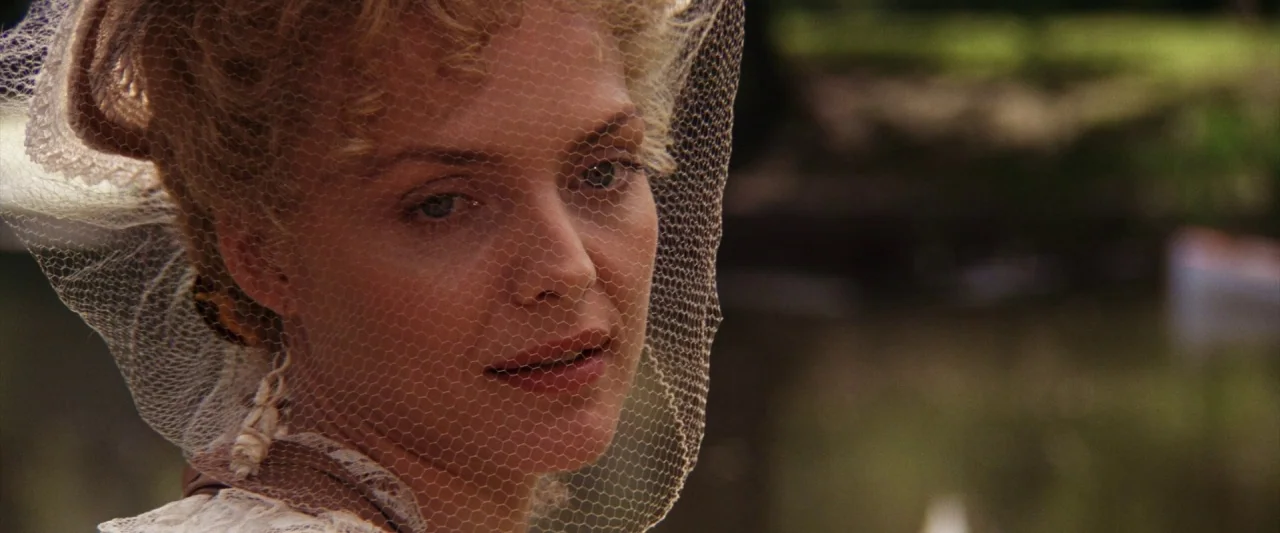 The Age of Innocence (1993) movie still: closeup — An outdoor park setting provides a blurred natural background of foliage and light. A woman with…