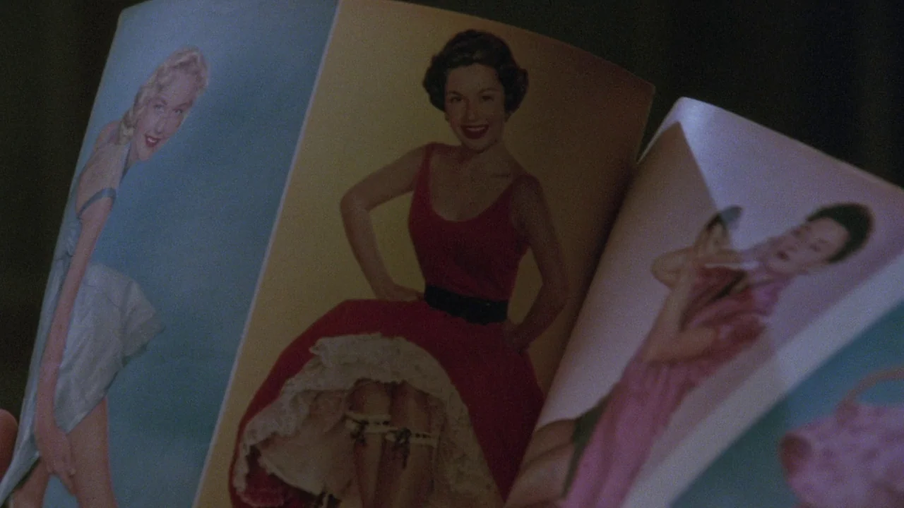 Insignificance (1985) movie still: closeup — An open magazine displays glossy printed photographs of women in vintage clothing. The paper pages are…