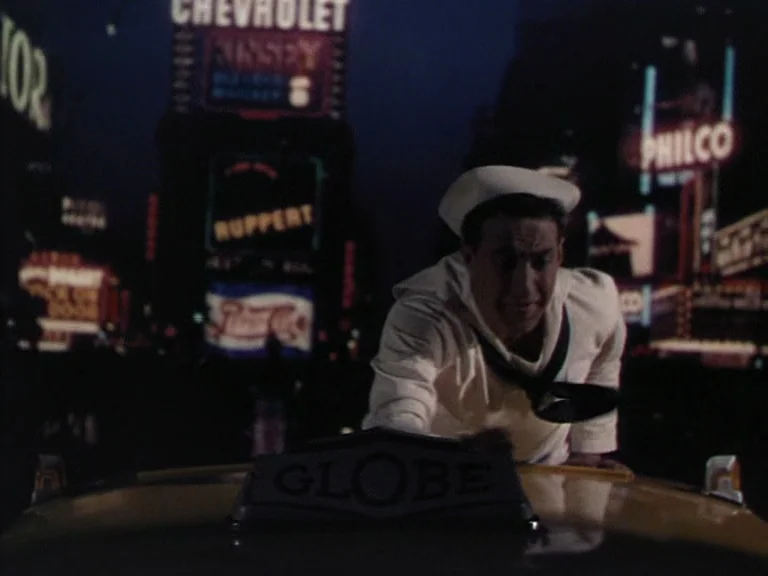 On The Town (1949) movie still: medium — A man in a sailor uniform leans over the roof of a taxi at night. Behind him are multiple bright glowing…