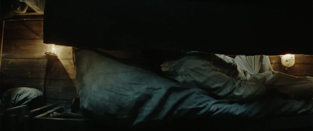 Sisu: Road to Revenge (2025) movie still: medium — A cramped wooden interior features a dark, narrow sleeping berth with exposed planks. A person…