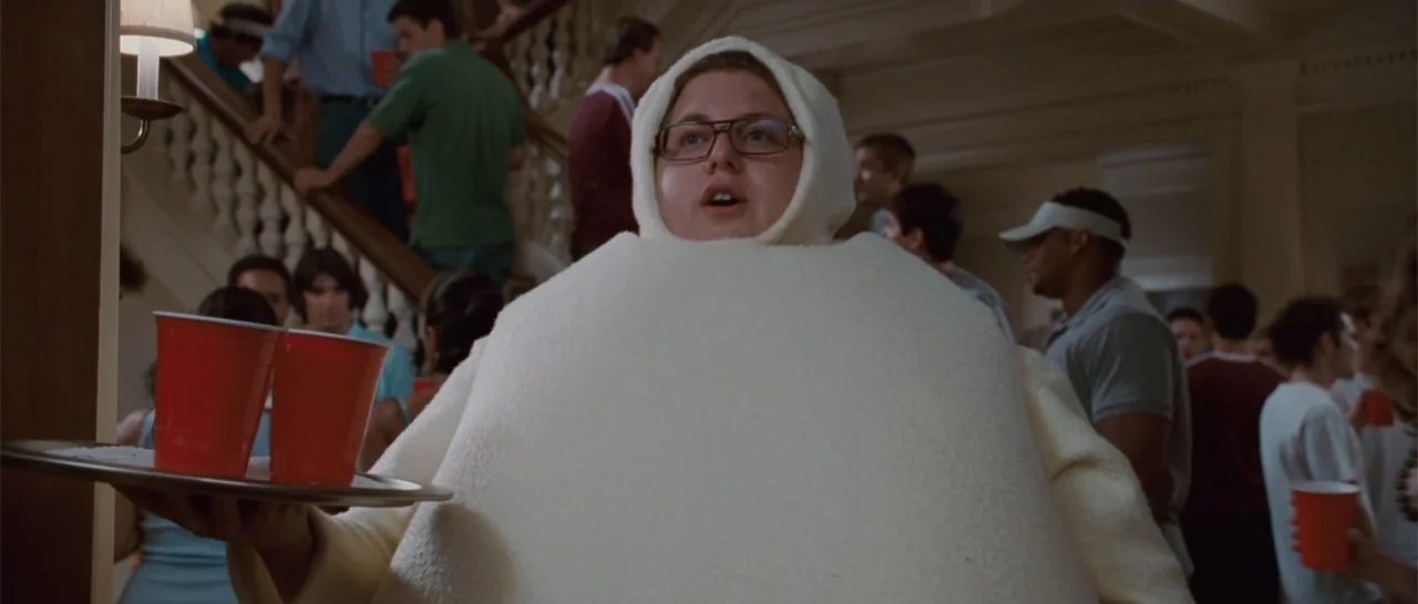 Accepted (2006) movie still: medium — A crowded fraternity house interior features a staircase and many young adult partygoers. A young man dressed…