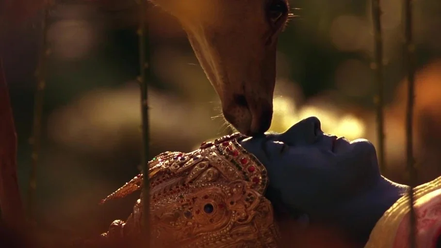 A Little Princess (1995) movie still: closeup — A deep blue-skinned figure wearing an ornate crown rests on the forest ground. A deer leans forward…