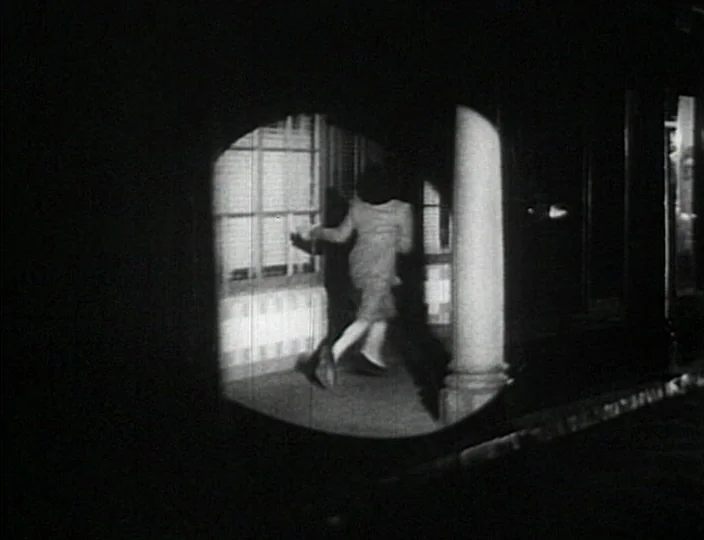 Dementia (Daughter of Horror) (1955) movie still: fullbody — A dark city street at night viewed through a circular vignette lens effect. A woman…
