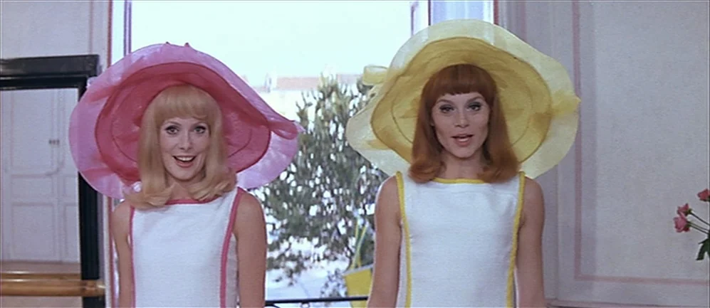 Les Demoiselles de Rochefort (1967) movie still: medium — A light-filled room with white walls and a large window view of trees. Two women stand…