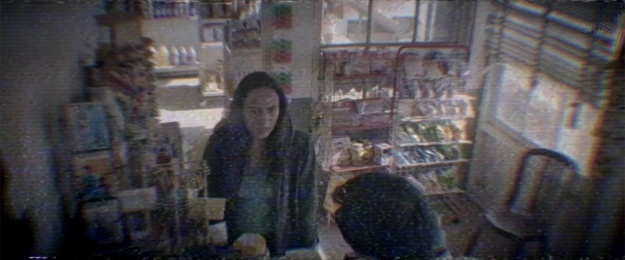 Truth or Dare (2018) movie still: medium — A small convenience store interior has shelves stocked with merchandise and a window with blinds. A woman…