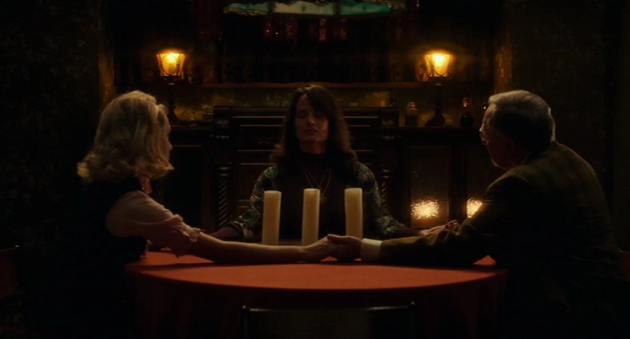 Ouija: Origin of Evil (2016) movie still: medium — A dimly lit room features a red-clothed round table with three upright white candles. Three…