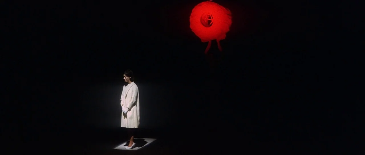 Tokyo Drifter (1966) movie still: wide — An expanse of deep black space contains a lone figure in white clothing. A bright red, textured circular…