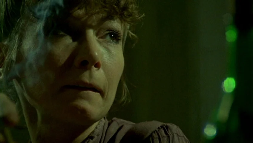 Almanac of Fall (1984) movie still: closeup — A dark interior setting is filled with a greenish haze. A woman looks off-camera while holding a…