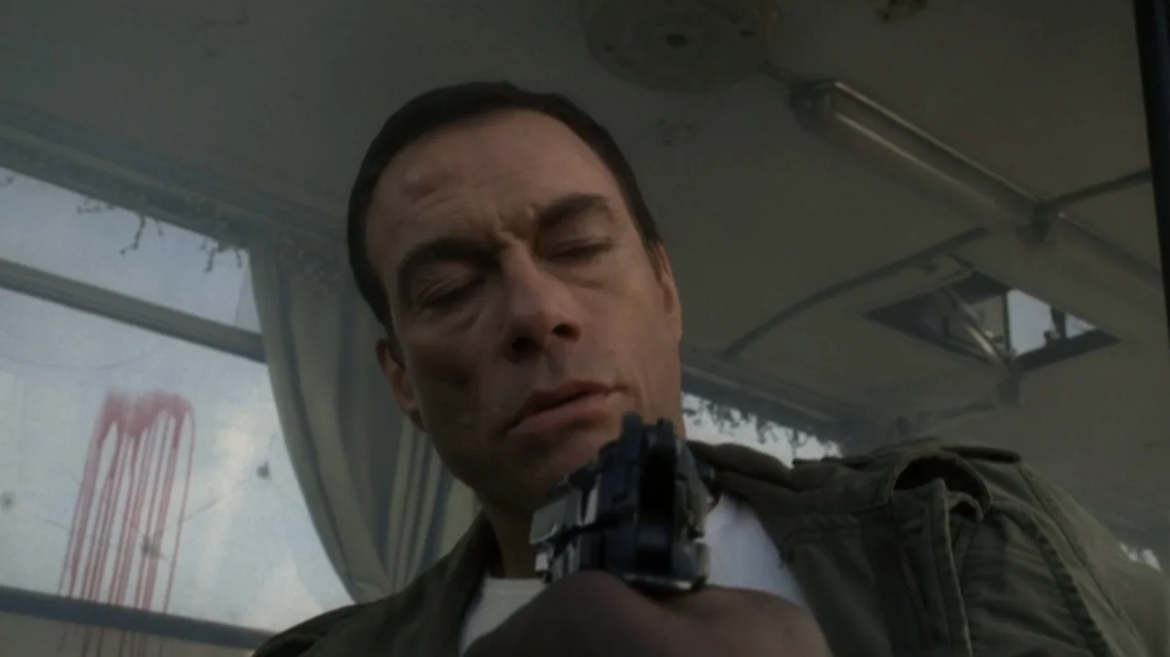 The Shepherd (2023) movie still: closeup — A cramped interior of a bus with a red blood streak on the window. A man holds a handgun while looking…