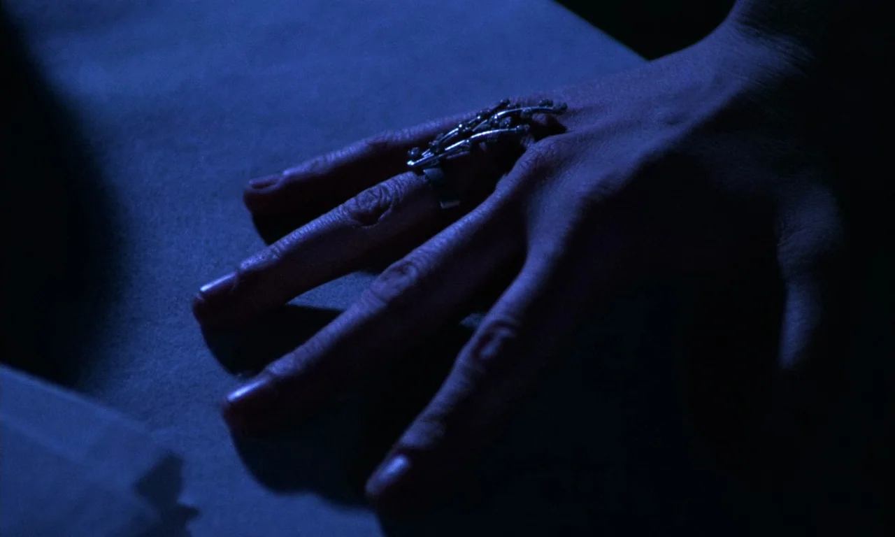 Demons 2 (1986) movie still: closeup — A close-up of a human hand resting on a flat, dark surface. The hand wears a complex, spiky silver ring on…
