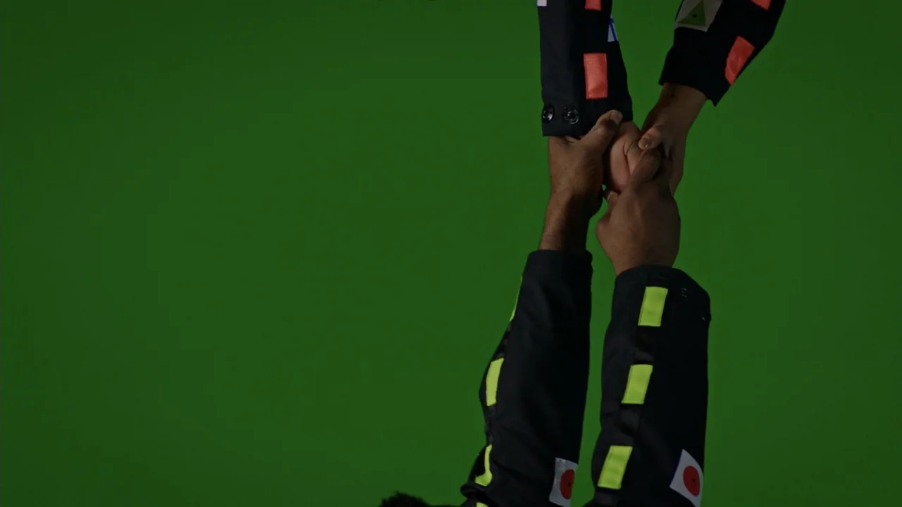 Die Hart (2023) movie still: closeup — A green screen studio background provides a blank digital workspace for visual effects. Two people in motion…