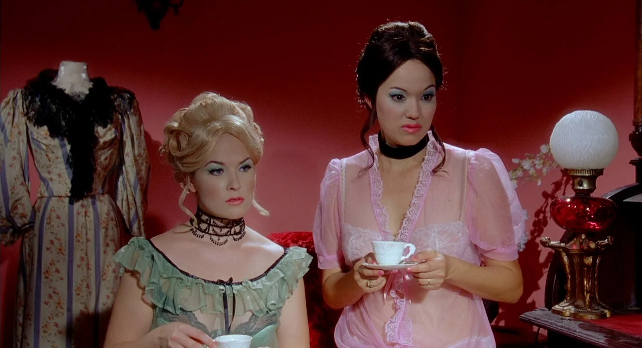 Viva (2007) movie still: medium — A dimly furnished room features a vibrant red wall and vintage decor elements. Two women in Victorian-style…