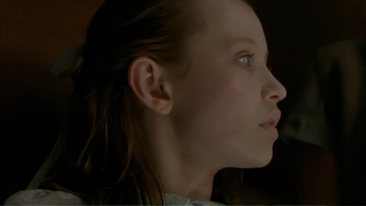 Ghost Ship (2002) movie still: closeup — A dimly lit room provides a dark, undetailed background for the subject. A young girl is captured in…