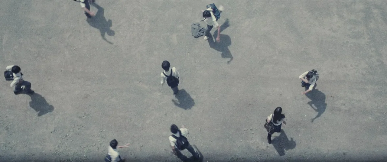 The World of Kanako (2014) movie still: establishing — A paved school courtyard area under bright sunlight with multiple students walking about.…