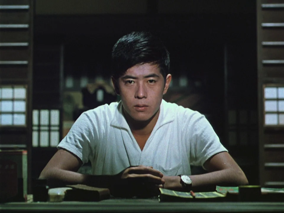 Floating Weeds (1959) movie still: medium — A traditional Japanese interior with paper screen doors framing the dark background. A young man sits…