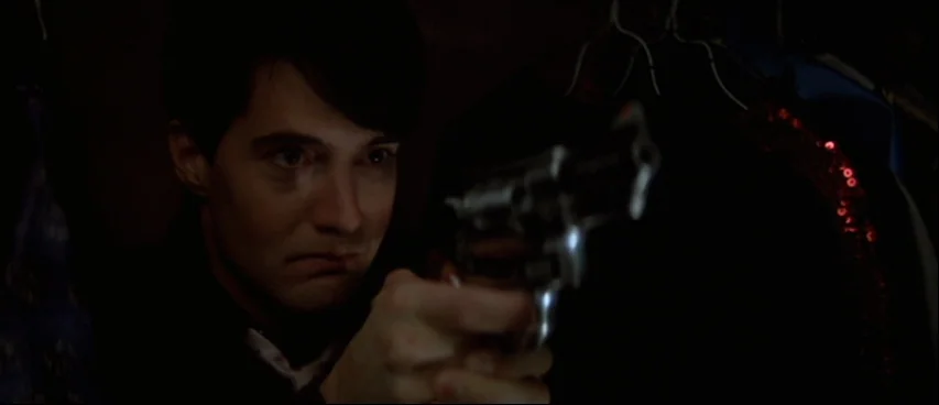 Blue Velvet (1986) movie still: closeup — A cramped closet filled with hanging clothes provides a dark, narrow space. A man points a revolver…