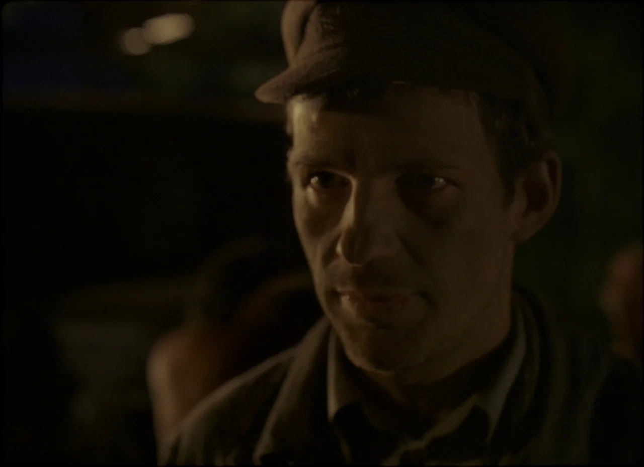 Son of Saul (2015) movie still: closeup — A dark, poorly lit environment with blurred, indistinct background shapes suggesting a busy public space.…