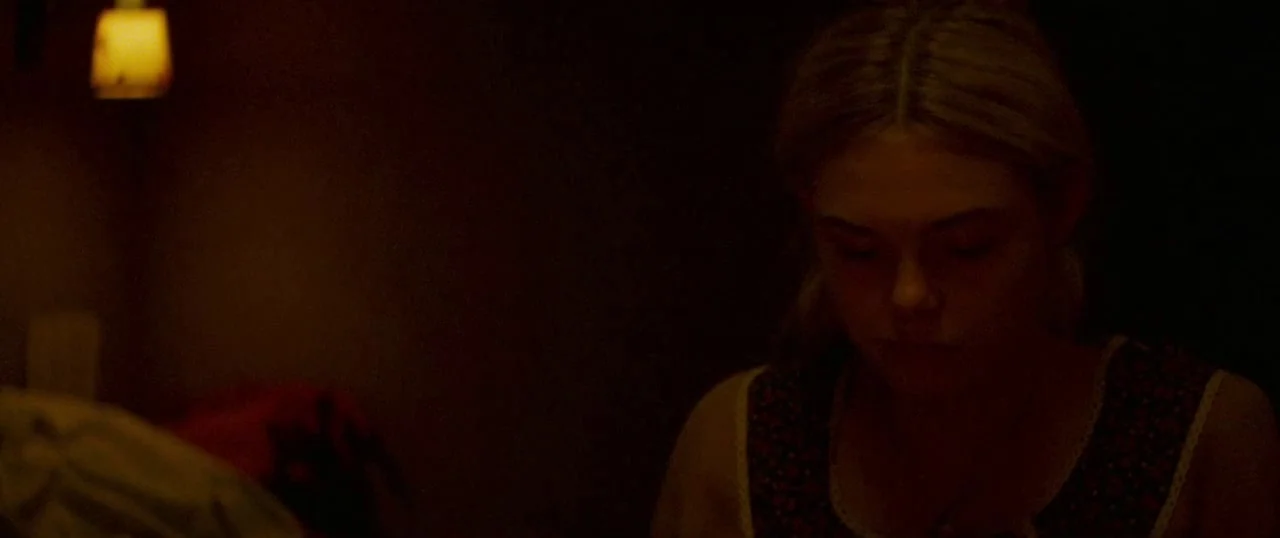 Low Down (2014) movie still: medium — A dimly lit room at night with minimal light from a nearby wall lamp. A young woman with blonde hair stares…