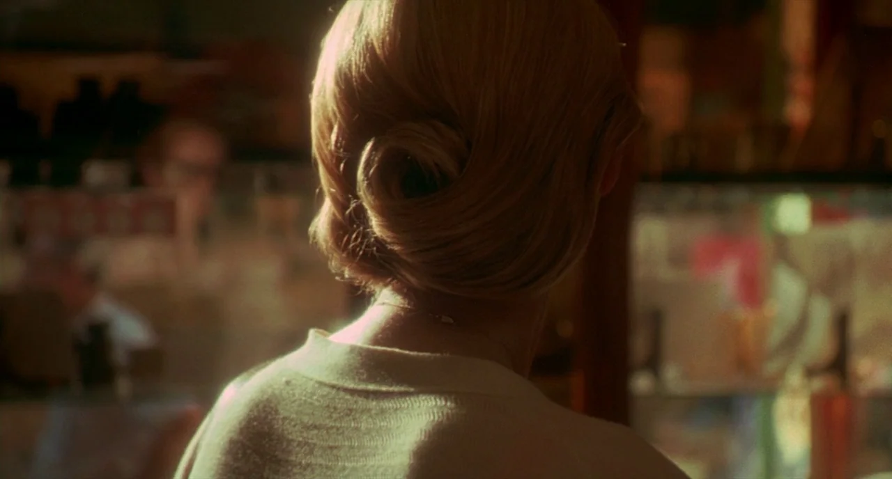 Making of: I Am Love (2009) movie still: closeup — A woman sits in a dim restaurant booth with soft golden light behind her. She faces away from the…
