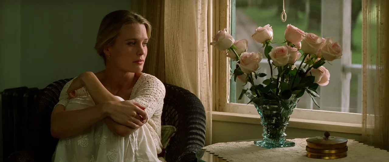 Forrest Gump (1994) movie still: medium — A light-filled sunroom features a wicker chair and a glass vase with roses. A blonde woman sits in the…