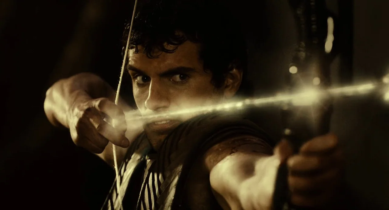The Immortals (2011) movie still: closeup — A dark, dimly lit environment obscures the background details behind the main subject. The man draws…