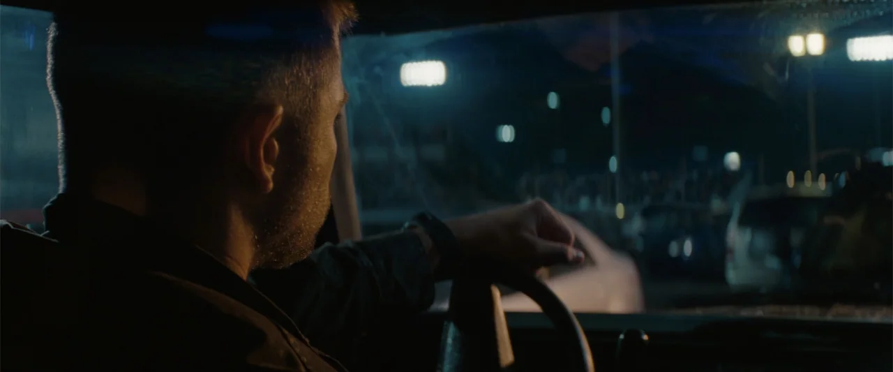 Red Dawn (2012) movie still: medium — The interior of a vehicle at night with blurred city lights visible through the windshield. A man in his…