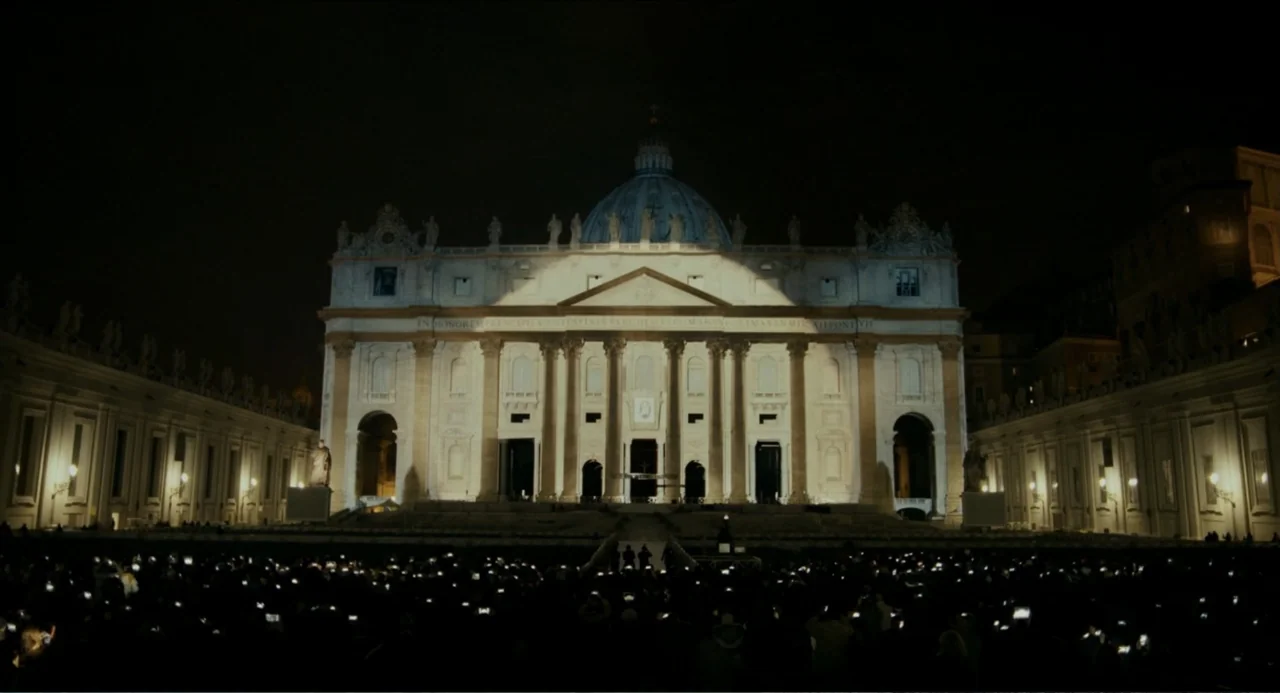Pope Francis: A Man of His Word (2018) movie still: establishing — St. Peter's Basilica at night with a large, dark crowd gathered in the…