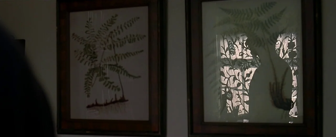 Little Children (2006) movie still: medium — Two wooden-framed prints hang side by side on a plain light-colored wall. A window with a decorative…