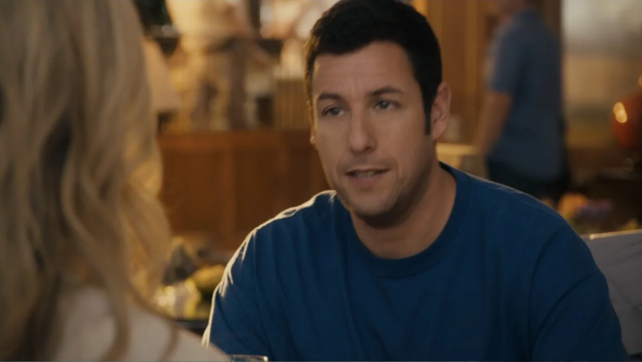 Just Go with It (2011) movie still: medium — An indoor restaurant setting with warm ambient lighting and blurred background figures. A middle-aged…