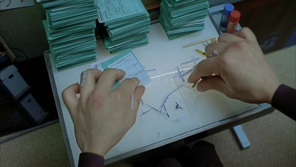 The Science Of Sleep (2006) movie still: closeup — A top-down view shows hands arranging small paper slips on a white desk surface. Piles of similar…