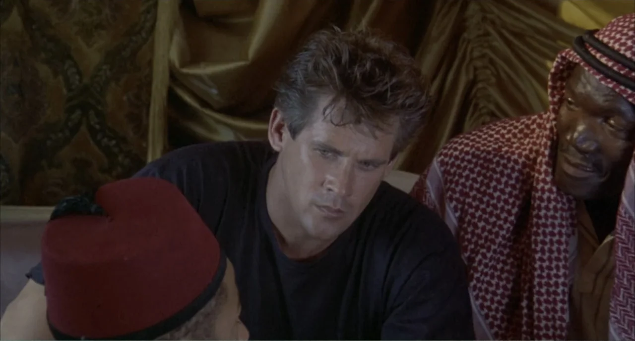 American Ninja 4: The Annihilation (1990) movie still: medium — A tent interior features draped gold and brown fabric backdrop walls. Two men in…