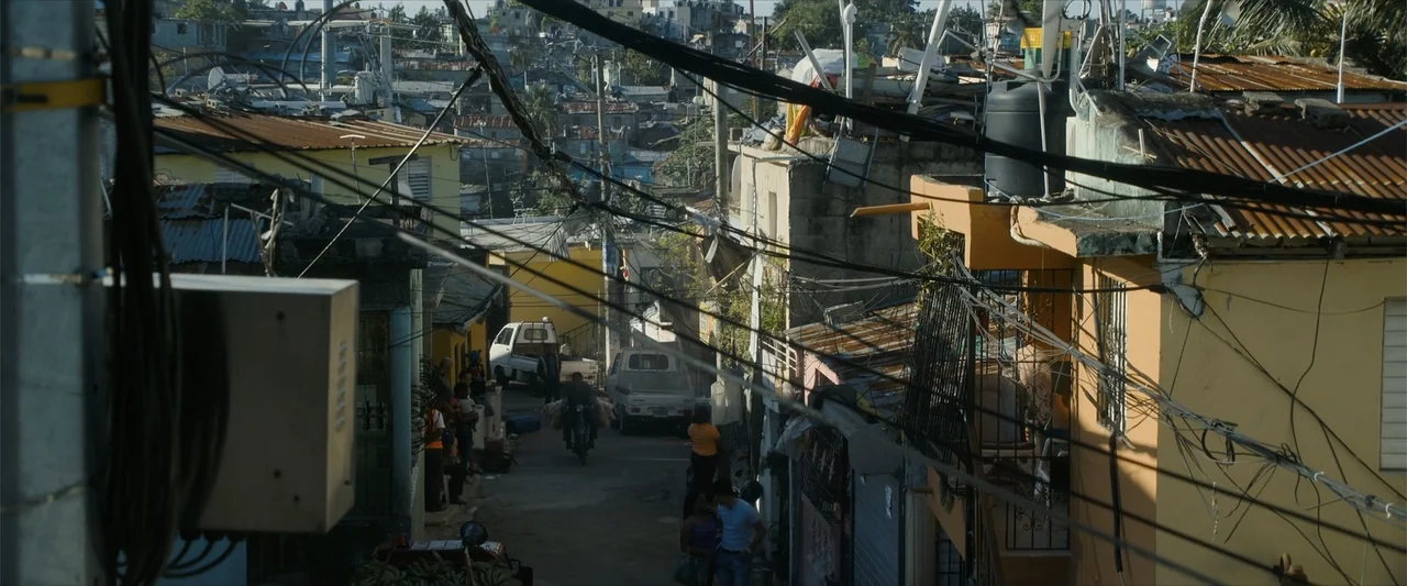 Arthur the King (2024) movie still: establishing — A dense urban neighborhood features closely packed multi-story buildings and complex overhead…