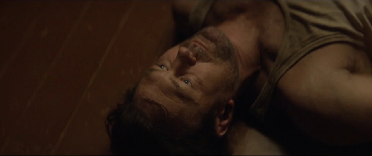 One & Two (2015) movie still: closeup — A man lies flat on a dark wooden floor in a dimly lit room. The subject is positioned horizontally across…