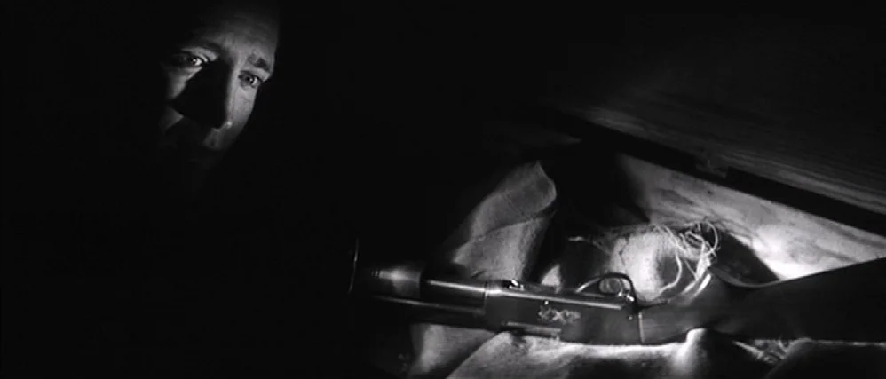 In Cold Blood (1967) movie still: closeup — A man stares into an open wooden container in a dark room. Inside the box rests a pump-action shotgun…