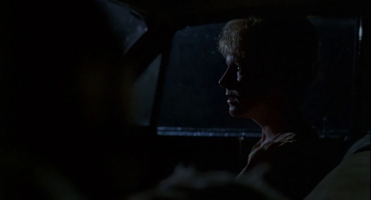 Psycho III (1986) movie still: medium — The interior of a car at night is dark with minimal ambient light. A woman is seen in profile while talking…