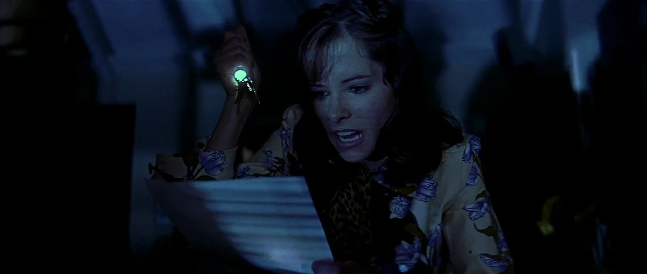 Scream 3 (2000) movie still: medium — The interior of a dark vehicle is lit only by a small, handheld flashlight. A woman wearing a floral jacket…